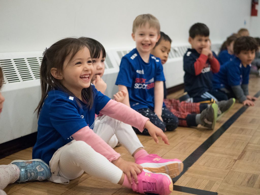 Five kids in soccer stars jerseys smiling while taking a break from soccer class.